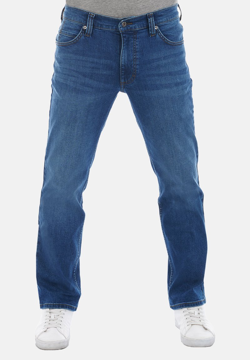 Jeans de mezclilla azul con un corte recto clásico, que cuentan con cinco bolsillos y un cierre de cremallera. Llevados con zapatillas blancas.