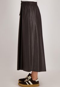Bruine neplederen maxi rok met een elastische tailleband en zijzakken, gedragen met donkere sneakers met witte accenten en veters.