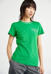 T-shirt verde in cotone con maniche corte, colletto bianco curvo e logo "PUMA" sul petto. Texture liscia, vestibilità casual.
