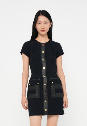 Navy dress with a fitted shape, short sleeves, gold buttons, and black leather pocket accents with geometric stitching details.
