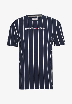 Granatowa koszulka z krótkim rękawem z białymi pionowymi paskami oraz logo „Tommy Jeans” z flagą w kolorach czerwonym, białym i niebieskim na środku klatki piersiowej.