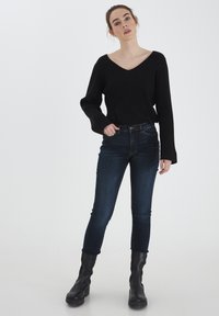 Suéter negro de punto acanalado con escote en V, combinado con jeans ajustados de lavado oscuro y botines negros. Diseño sencillo, silueta ajustada.