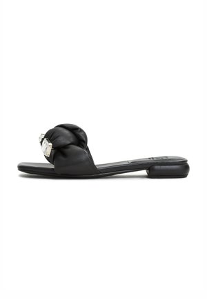 Sandal in pelle nera con parte superiore annodata e un accento decorativo in argento. Suola piatta con tacco minimo, texture liscia.