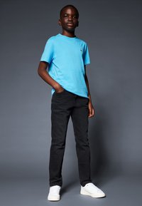 Modrá bavlnená tričko, čierne džínsy a biele tenisky. Tričko má malé logo na ľavom hrudníku. Jednoduchý, neformálny outfit.