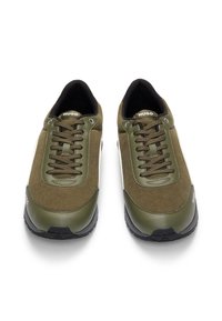 Pár olivově zelených volnočasových tenisek se šňůrkami, černými podrážkami a logem "HUGO" na jazyku a boku, pohled zepředu.
