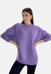Fioletowy dzianinowy sweter o luźnym kroju, z prążkowanym dekoltem i szerokimi rękawami. Posiada teksturowane wykończenie i sięga do bioder.