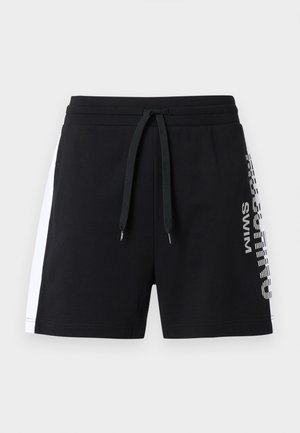 Melni peldbikses ar baltām sānu panelēm, regulējamu auklu viduklī un vertikāli drukātu uzrakstu "Chill Swim" labajā kājā.