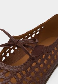 Chaussure en cuir marron avec texture tissée et lacet décoratif noué sur la partie supérieure, montrant les détails intérieurs et latéraux.