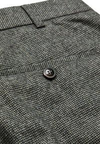 Grau Hahnentrittmusterstoff mit einem großen schwarzen Knopf am Bund und einer strukturierten Oberfläche mit feinen Details.