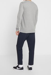Haut gris à manches longues côtelé associé à un pantalon slim bleu marine et des baskets noires. La tenue présente un design décontracté et confortable.