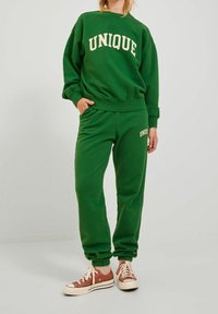 Sudadera verde y joggers a juego, ambos con la palabra "ÚNICO" en crema, hechos de material suave con puños y cinturilla elásticos.