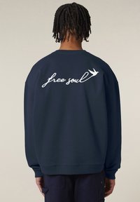 Sudadera blu navy con taglio oversize, caratterizzata da testo bianco ricamato 'free soul' e un motivo di uccello sul retro. Texture morbida e stile minimalista.