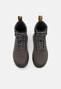 Paire de bottes montantes gris foncé avec lacets noirs et blancs, semelles noires, et languettes jaunes de marque à l'arrière.