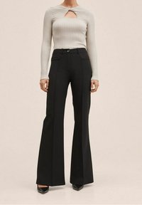 Szary prążkowany top z długim rękawem z wycięciem na karku, zestawiony z czarnymi, dzwonowatymi spodniami z wysokim stanem. Gładka faktura i dopasowany krój.