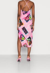 Robe rose à motifs avec des bretelles fines et ajustables, présentant des imprimés graphiques et une fente latérale. Associée à des sandales à talons roses.