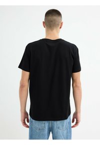Camiseta de algodón negra de cuello redondo con mangas cortas, corte relajado y textura suave. La vista trasera muestra un dobladillo recto y detalles de costura.