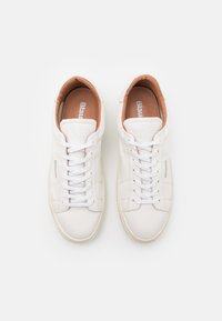 Sneaker bianche in pelle con una texture liscia, punta tonda e design low-top. Presentano lacci bianchi e un interno beige con marchio stampato.