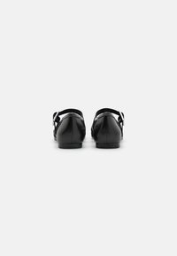 Black leather shoes with a low heel, adjustable strap, and silver buckle detail. Smooth texture, rounded toe, minimalist design.