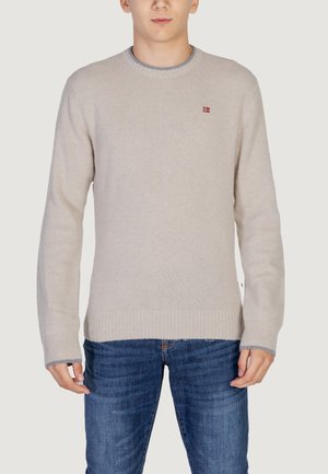 Beige sweater with a crew neck and ribbed cuffs. Features a small red logo on the chest. Worn with blue jeans. Soft texture.
