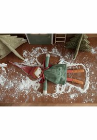 Soft fabric doll with a red pointed hat, green dress, and orange limbs, lying in a flour dust pattern on a brown wooden surface.
