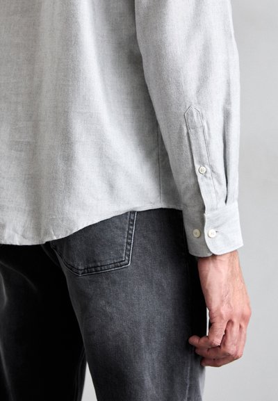 Ljusgrå långärmad skjorta med knappslut, som matchas med mörkgrå jeans. Tyget verkar ha en texturerad och avslappnad stil.