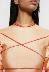 Top de cetim na cor pêssego com detalhes em ponto cruz vermelho e gola alta. Textura suave com mangas curtas.