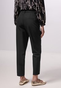 Schwarze taillierte Hose mit schmalem Schnitt, ausgestattet mit seitlichen Taschen und einer glatten Textur, kombiniert mit metallischen Flachschuhen.