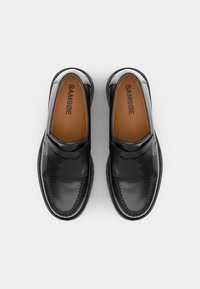 Black leather slip-on shoes with a smooth finish, featuring a rounded toe, decorative strap across the front, and a contrasting brown insole.