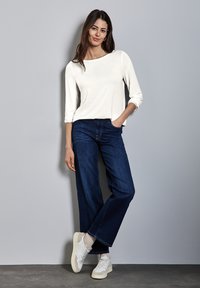 Chemise blanche à manches longues associée à un jean large bleu foncé, avec une coupe décontractée et des manches retroussées, complétée par des baskets blanches.