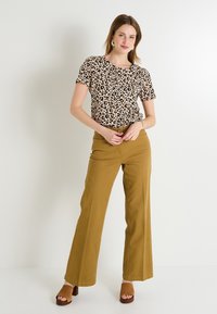 Top de manga corta de estampado de leopardo combinado con pantalones de pierna ancha mostaza y sandalias de tacón marrón. Accesorio: pendientes en forma de estrella.