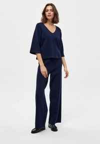 Completo due pezzi blu navy con scollatura a V, maniche ampie e pantaloni larghi. Realizzato in un tessuto morbido e testurizzato con una silhouette relaxed.