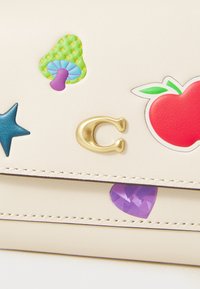Cream-colored leather purse featuring colorful stickers: green mushroom, red apple, blue star, and a gold "C" accent.