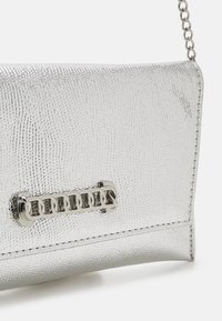 Petit sac à main argenté texturé avec une bandoulière chaîne en métal et un détail décoratif de maillon de chaîne sur le rabat avant.