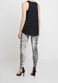 Top nero senza maniche abbinato a leggings aderenti con un motivo a squama di serpente bianco e nero. Scarpe nere con tacco alto.