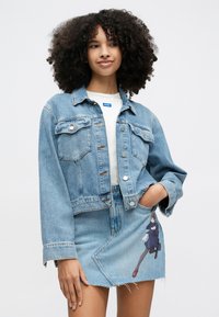 Ανοιχτό μπλε τζιν μπουφάν με κουμπιά και τσέπες, συνδυασμένο με φούστα από ανοιχτό μπλε τζιν με εκτυπωμένο σχέδιο χαρακτήρα.