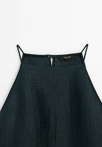 Robe en lin vert foncé avec des bretelles fines ajustables, une fermeture à boutons dans le dos, et une finition de tissu légèrement texturée.