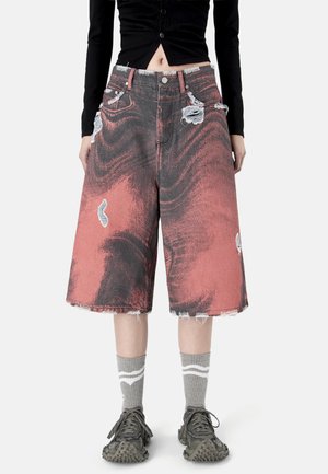 Szorty dżinsowe z szerokimi nogawkami, postrzępione, w czarnym i wyblakłym czerwonym kolorze, zestawione z szarymi skarpetkami i czarnymi teksturowanymi tenisówkami.