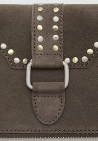 Portefeuille en daim gris avec une large sangle ornée de clous métalliques et une fermeture argentée. Des coutures détaillées et une texture lisse mettent en valeur le design.