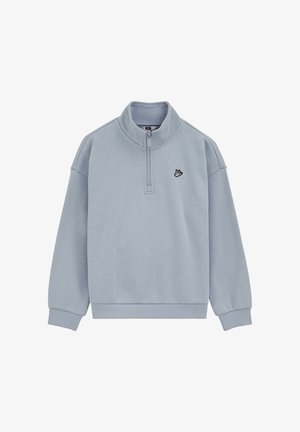 Lichtblauwe pullover met kwartrits, geribbelde manchetten en zoom, en een klein zwart-wit geborduurd logo op de linkerborst.