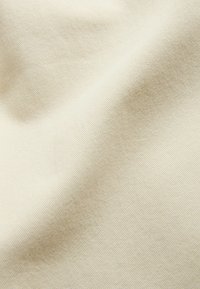Tissu beige clair avec une texture fine de tissage diagonal et des plis doux créant des ombres et des reflets.