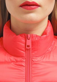 Röd puffjacka med hög krage och slät yta. Har en central dragkedja med "HILFIGER"-logotyp på dragknappen.