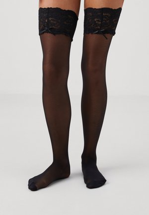 Bas noirs montants jusqu'à la cuisse, avec une dentelle sur le dessus à bords festonnés, une texture lisse et des nœuds décoratifs au bord en dentelle.