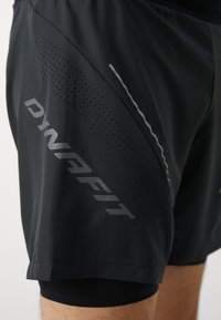 Shorts de sport noirs avec une texture légère et lisse. Comprend des panneaux en mesh, des accents réfléchissants et un logo de marque bien visible.