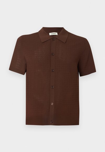 Καφέ κοντομάνικο πουκάμισο με κουμπιά, υφασμένη υφή και κλασικό γιακά, παρουσιάζεται σε απλό ανοιχτό φόντο.