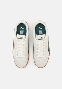 Egy fehér bőr felsőrészes sneaker zöld részletekkel a nyelvén, és barna gumitalppal. Fűzőkkel és Puma logóval a oldalán.
