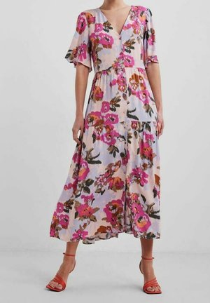 Frau trägt ein Midikleid mit floralem Muster in Pink, Orange und Braun, mit Puffärmeln, V-Ausschnitt und orangefarbenen Riemchenabsätzen vor einfachem Hintergrund.