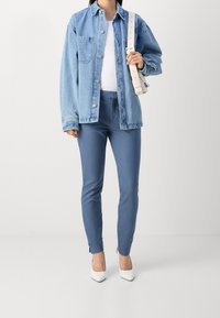 Světle modrá džínová bunda, bílý top, modré elegantní kalhoty a bílé špičaté podpatky; má uvolněný střih, knoflíky a jemné akcenty.