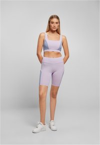 Conjunto deportivo en un suave tono púrpura claro que incluye un top corto con escote cuadrado y pantalones cortos con paneles laterales en un tono más claro; textura suave.