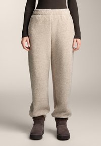 Bež, puhast džogerske hlače iz flisa z elastičnim pasom in zaključki z gumijastim robom. V kombinaciji s temnimi, mehkimi gležnjarji.