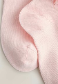 Lyserøde sokker lavet af ribstrikket stof med en blød, glat tekstur, rundet tå-sømme og en delikat blomsterdetalje.